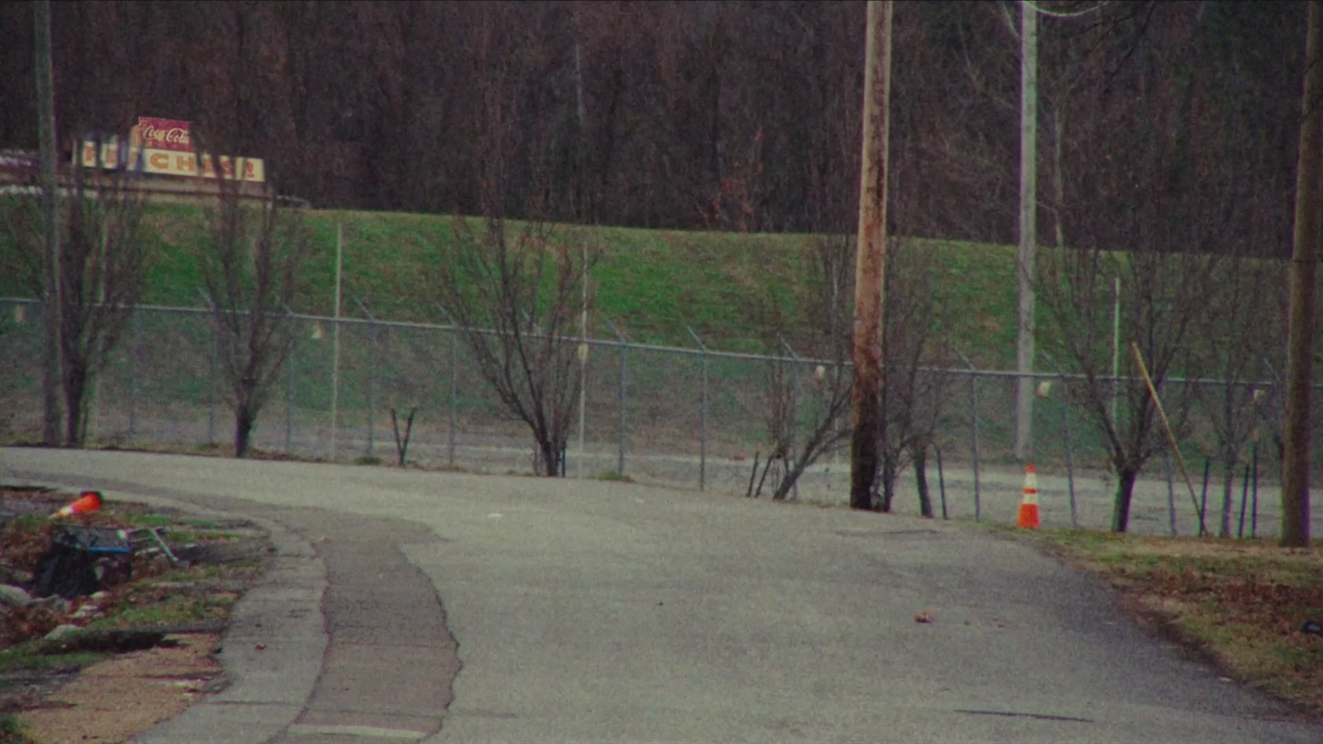 Vintage video of the band members driving a red 1970s two door car down a backroad with powerlines 